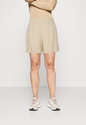 Shorts beige clair en tissu doux avec une taille élastique, présentant une coupe droite et des poches latérales. Portés avec des chaussures de sport beige.
