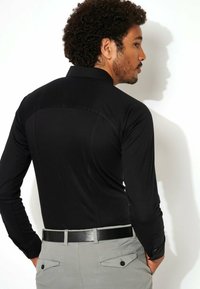 Zwarte langesleeve shirt met een gladde textuur, voorzien van een button-down kraag en een getailleerd ontwerp, gecombineerd met lichtgrijze broeken en een zwarte riem.
