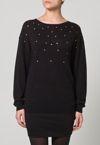 Schwarzes Pulloverkleid aus Strickstoff mit lockerem Sitz, langen Ärmeln und verstreuten goldenen Nieten auf der Vorderseite zur Verzierung.