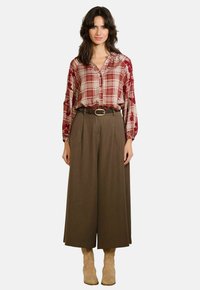 Rood en beige geruite blouse met geborduurde bloemen op de mouwen, gecombineerd met high-waisted bruine wijde broek en beige enkellaarsjes.