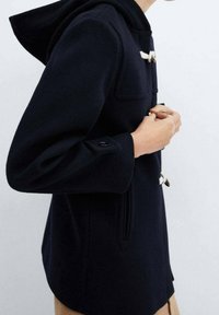 Cappotto in lana blu navy con cappuccio, dotato di chiusure a langetta, tasche laterali e una vestibilità comoda. La manica include un dettaglio con bottone.