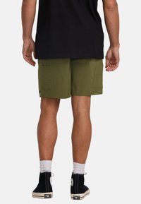 Pantalones cortos de carga verdes con dos bolsillos laterales, hechos de tejido ligero. Combinados con una camiseta negra y zapatillas altas negras.
