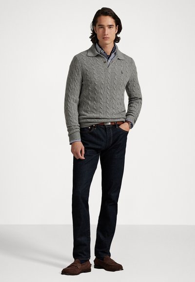 Pull en tricot gris avec col, associé à un jean bleu marine et des chaussures en suède marron ; présente une coupe ajustée et des poignets côtelés.