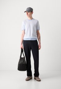 Top corto a maniche corte di colore azzurro chiaro con orlo a costine, pantaloni neri su misura, berretto grigio, in mano una borsa di tessuto nera e sneaker beige.