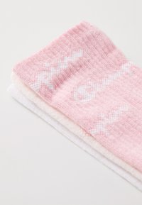 Calcetines rosa y blancos doblados juntos, con un tejido texturizado, donde el calcetín rosa tiene un patrón en zigzag y el calcetín blanco es liso por debajo.