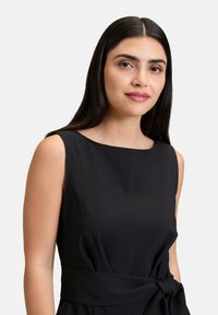 Fekete ujjak nélküli ruha kerek nyakkivágással, oldalsó megkötő részlettel a deréknál, sima anyagból készült, testhezálló fazonnal.