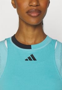 Aquamarijn atletisch tanktop met mesh accenten. Heeft een ronde halslijn en een zwart logo op de borst. Getextureerde stof, aansluitend ontwerp.