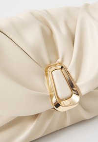Beige faux leren clutch met geplooide textuur, met een opvallend gouden metalen sluitingdetail aan de voorkant.