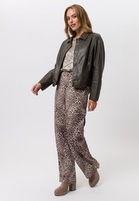 Veste en cuir marron sur un haut beige avec des embellissements, associée à un pantalon large à imprimé léopard et des bottes à talons marron clair.