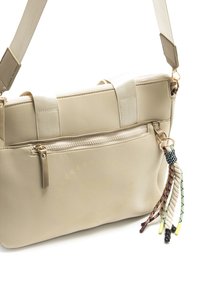 Sac à main beige avec une surface texturée, une poche zippée à l'avant et des pompons décoratifs de différentes couleurs. Comprend des sangles réglables et amovibles.