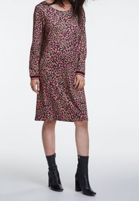 Robe imprimée léopard avec des accents roses, manches longues et décolleté rond. Fabriquée en tissu doux, avec des poignets côtelés. Portée avec des bottines noires.