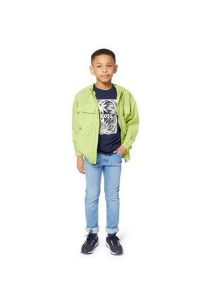 Enfant portant une veste à capuche vert clair par-dessus un t-shirt bleu marine avec un design de palmier, assortie à un jean bleu clair et des baskets noires.
