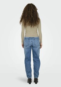 Maglione lungo a maniche lunghe di un beige chiaro a coste e jeans in denim blu sbiadito a vestibilità rilassata con due tasche posteriori, indossati con stivali neri con tacco.