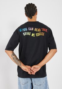 Svart bomulls T-skjorte med korte ermer, med fargerik tekst bak: "HVIS DU KAN LÆSE DETTE, FOR MY COFFEE." Standard passform.