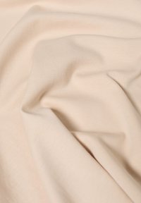 Tissu extensible beige avec une texture lisse, présentant des plis et rides subtils, mettant en valeur sa nature flexible et douce.