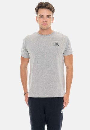 Homme faisant face à l’avant portant un t-shirt gris clair avec le logo "LEONE 1947" et un pantalon noir avec le texte "LEONE" sur la cuisse gauche.