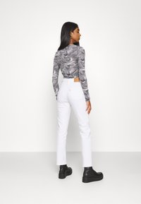Long-sleeve shirt with black and white marble pattern, paired with high-waisted white jeans and black ankle boots. Back view of outfit.