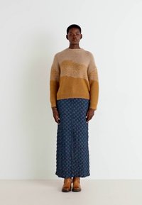 Stickad tröja i beige och dämpade bruna nyanser, med en strukturerad design; tillsammans med en lång, mörkblå kjol med diamantmönster. Bruna ankelstövlar.