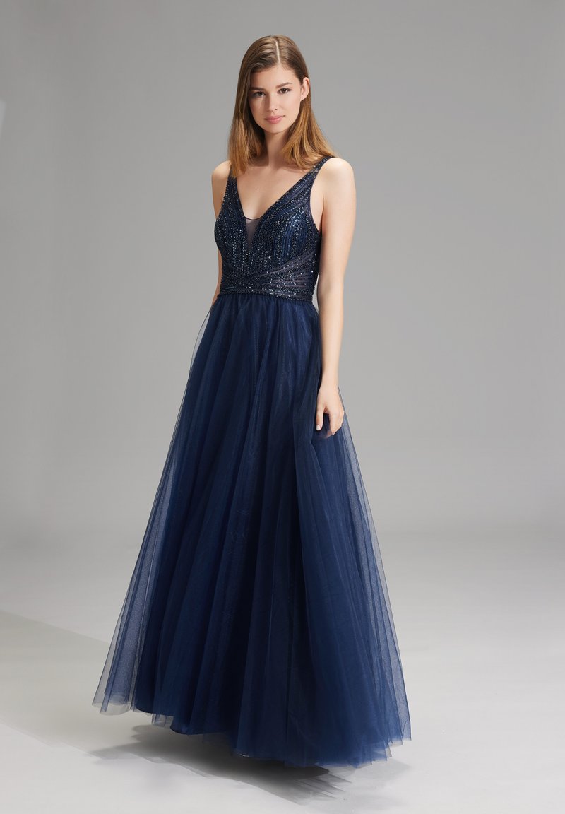 Abito da sera blu navy con un corpetto aderente ricoperto di perline e una gonna in tulle fluente. Il design con scollatura a V presenta spalline larghe e dettagli di lieve lucentezza.