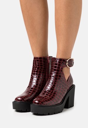 Burgundské lakované kotníkové boty s krokodýlím vzorem, bočními prořezy, sponou a masivní černou platformou.