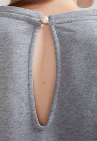 Grå stickad topp med en nyckelhålsöppning bak, säkrad med en pärlkull. Slät textur och avslappnad passform.