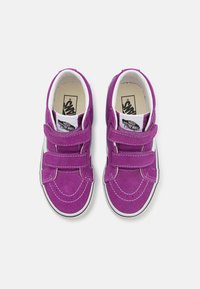 Lilla nahkaskoorega sneakers kahe Velcro rihmaga, valge õmblusega ja musta-valge logoga keelel. Lame kummist tald.