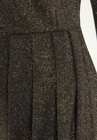 Svart klänning med en texturerad tyg med guldprickar. Den har veck för extra volym och en figursydd bodice-design.