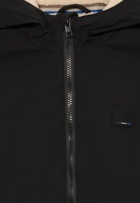 Sudadera con cremallera negra y superficie texturizada, con un interior suave, capucha ajustable y un pequeño parche de marca en el pecho.