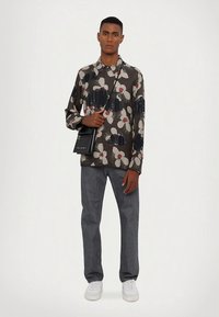 Košulja na kopčanje s cvjetnim uzorkom u tamnim tonovima, s dugim rukavima i opuštenim krojem, uparena s sivim trapericama. Crna torbica na remenu preko tijela upotpunjuje izgled.