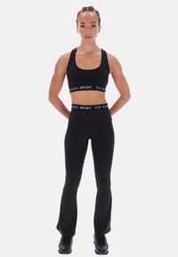 Čierny športový podprsenka a legíny s vysokým pásom a kontrastným nápisom na páske. Hladký, elastický materiál s priliehavým strihom. Čierne tenisky.