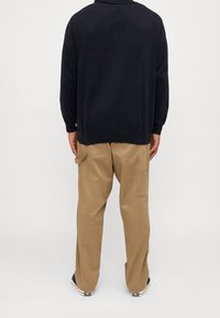 Pull noir à manches longues avec poignets côtelés, associé à un pantalon cargo beige avec poches latérales et coupe décontractée.