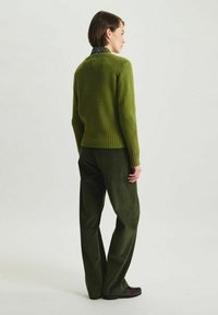 Pull en tricot vert avec un ourlet côtelé, assorti à un pantalon en velours côtelé vert foncé. Le pull présente un design simple et un tricot texturé.