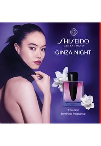 Shiseido Ginza Night parfyme i en klar flaske med en lilla gradient, toppet med et svart lokk, mot en lilla bakgrunn med hvite blomster.