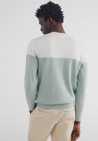 Hellgrüner und cremefarbener Farbblock-Pullover, gestrickte Textur, runder Ausschnitt, gerippter Saum und Manschetten, kombiniert mit beigen Hosen.