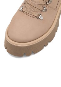 Svetlo béžová turistická obuv s hladkým koženým zvrškom, hrubou hnedou podrážkou, štruktúrovanými šnúrkami a kovovými okami. Masívny dezén na podrážke.