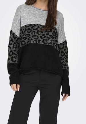 Femme portant un pull color block avec des panneaux gris, noir et imprimé léopard, associé à un pantalon noir.