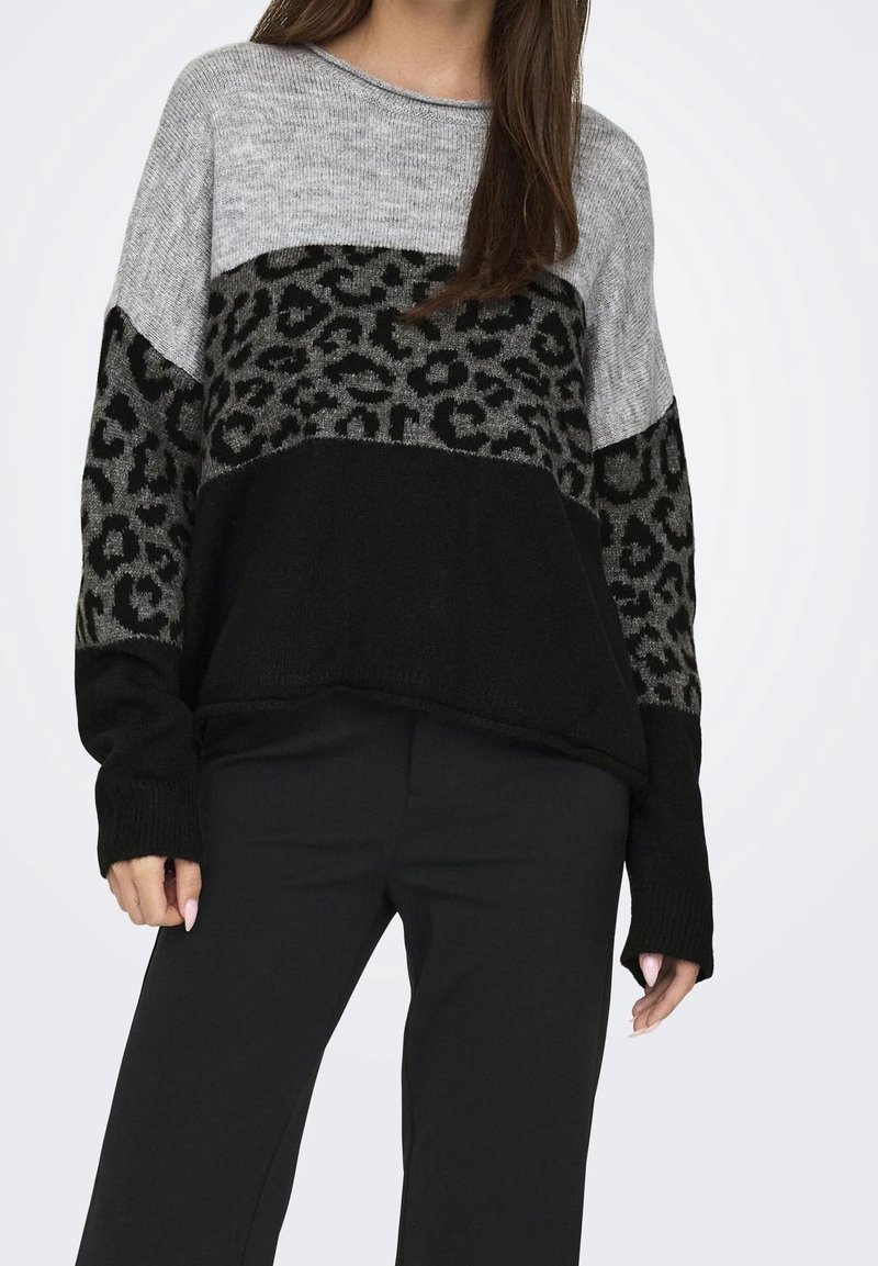 Femme portant un pull color block avec des panneaux gris, noir et imprimé léopard, associé à un pantalon noir.