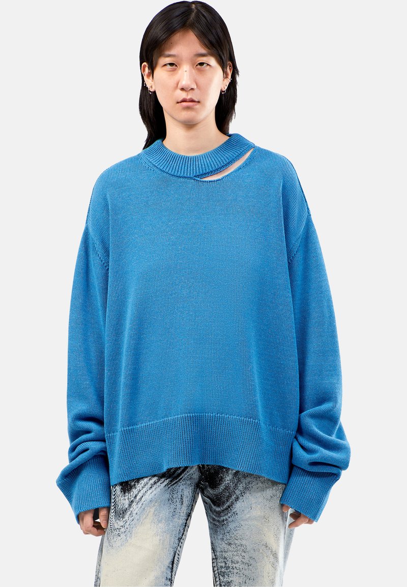 Blue knit sweater with a wide neckline and a cutout detail. Features loose sleeves and a ribbed hem. Worn with light, patterned jeans.