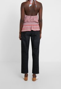 Red and blue patterned halter-top with a ruffled hem, paired with dark denim pants. The top features a tie detail at the neck.