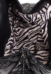 Black quilted handbag featuring a spacious interior lined with beige and dark purple zebra print fabric. Includes a silver chain detail zipper.