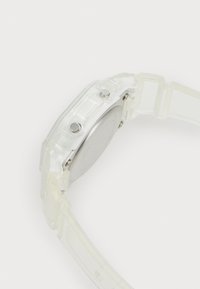 Gennemsigtig plastikklokke med en bagside i sølvfarvet rustfrit stål. Har to knapper på siden, fleksibel rem og rektangulær form.