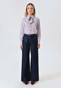 Witte shirt met rode verticale strepen en een strikseen, gecombineerd met donkerblauwe wijde spijkerbroek met voorzakken.