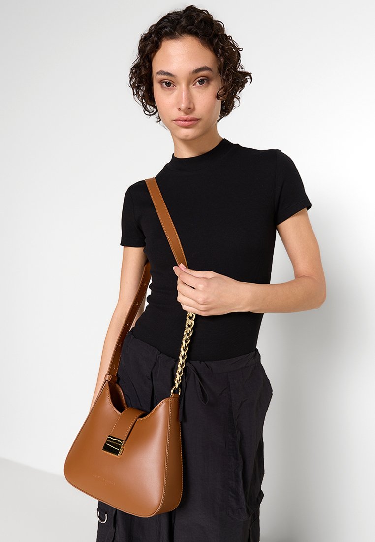Sac à main en cuir marron avec une silhouette décontractée, présentant une chaîne en métal doré et un fermoir magnétique à l'avant. Surface texturée.