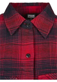 Col de chemise à carreaux rouges et noirs, boutonné, avec boutons noirs et étiquette Urban Classics XS visible à l'intérieur.