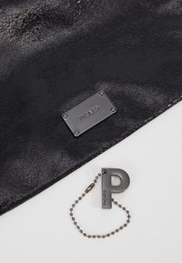 Article en cuir noir texturé avec une plaque de marque rectangulaire en métal "PICARD" et un porte-clés en métal en forme de lettre P sur une chaîne à billes.