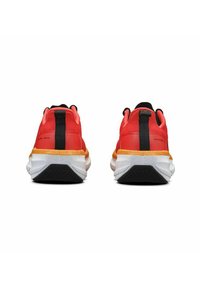 Rode sportschoenen met een zwarte streep en gele accenten. Dikke witte zolen met een gestructureerde zwarte rubberen onderkant. Achteraanzicht, toont het ontwerp van de hak.