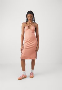Robe midi en pêche côtelée avec col halter, détail en trou de serrure et fentes latérales, associée à des baskets roses avec des rayures blanches et une semelle en gomme.