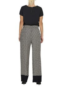 Haut noir à manches courtes associé à un pantalon à taille haute à motifs noir et blanc, avec une coupe évasée et un accent bleu marine à l'ourlet.
