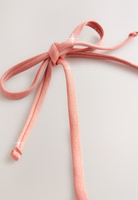 Lyserødt stofbånd bundet i en knude med to lange, teksturerede ender. Materialet har en let glans, der giver det en subtil glimt.