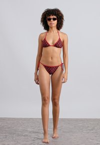 Rød og sort bikini-sett med trekantet topp med justerbare knytebånd og matchende lavskårede truser med sidesnøring. Glatt tekstur.
